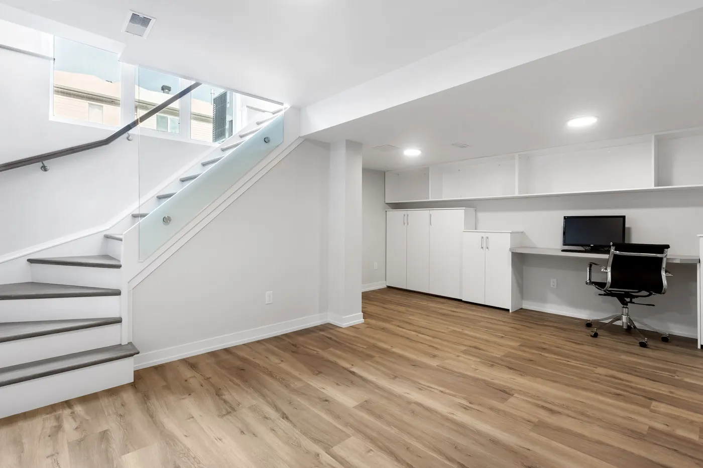 A finished basement with a home office, wood-look floor and white walls