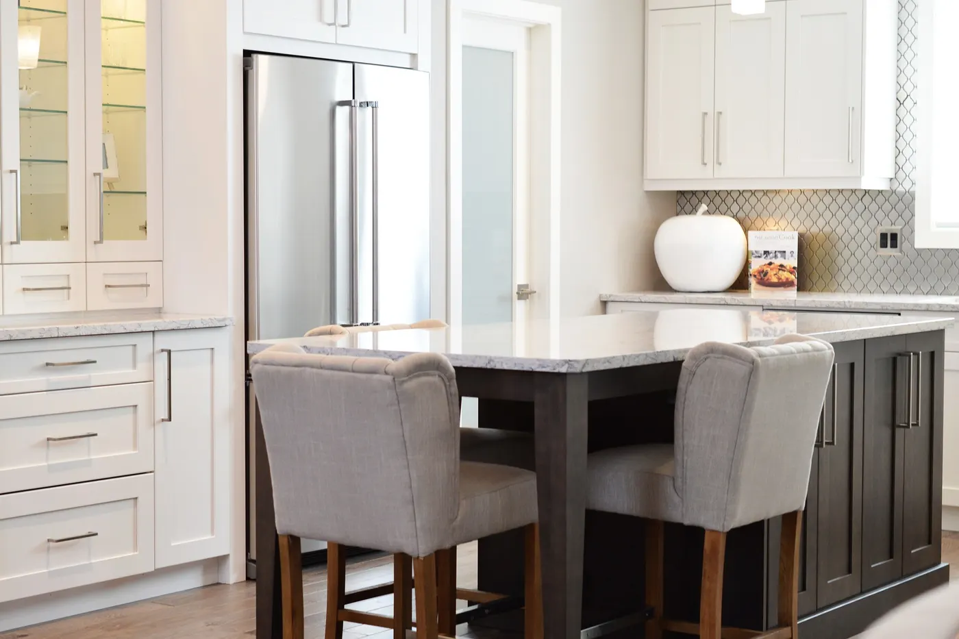 A white kitchen with a dark island and upholstered bar stools