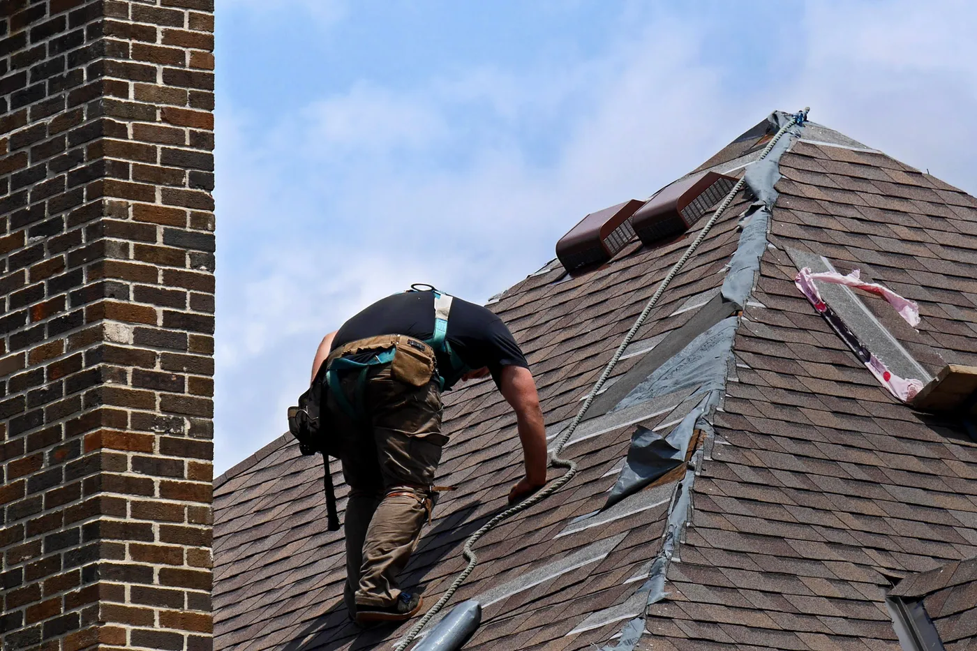 A roofer working along the hip of an asphalt shingle roof