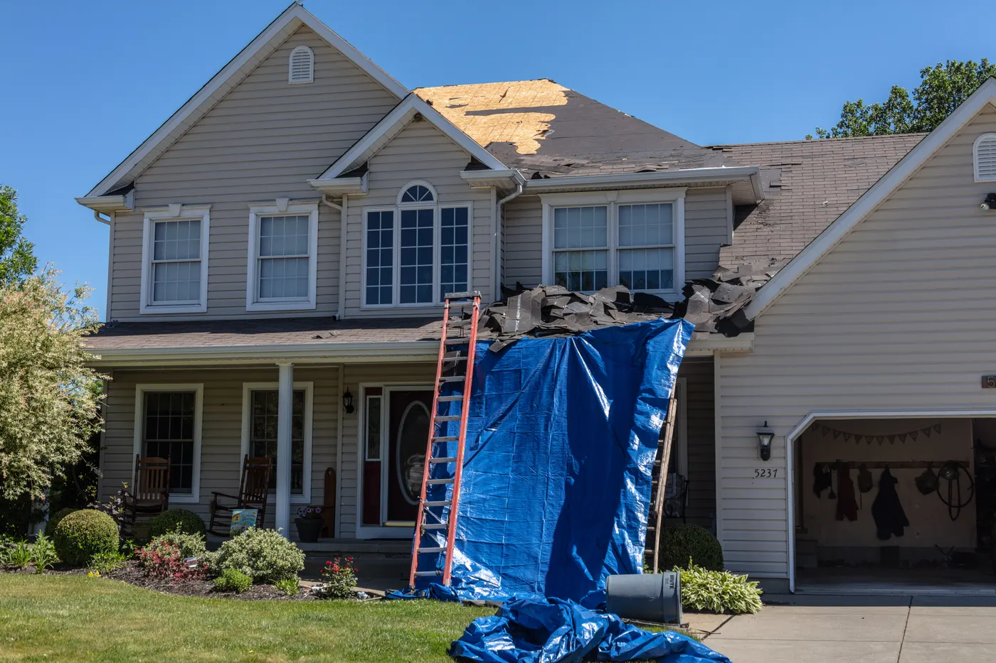 A storm-damaged roof covered with a tarp on a two-story home