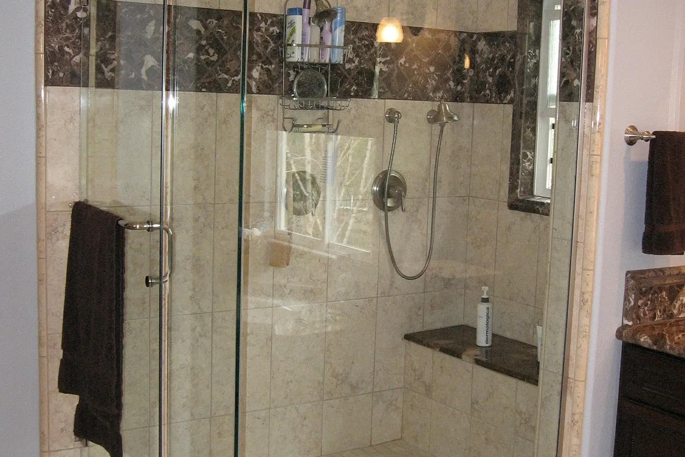 A tiled shower with a glass door and a recessed shelf